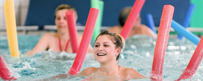 Frauen machen Wassergymnastik mit roten, grünen, orangenen und blauen Schwimmnudeln