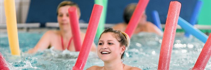 Frauen machen Wassergymnastik mit roten, grünen, orangenen und blauen Schwimmnudeln