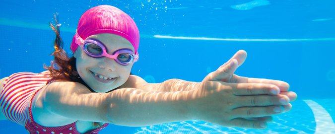 Ein junges Mädchen taucht mit Schwimmbrille unter Wasser.