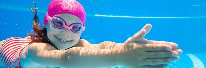 Ein junges Mädchen taucht mit Schwimmbrille unter Wasser.