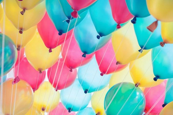 Luftballone in blau, gelb und rosa fliegen dicht beieinander.