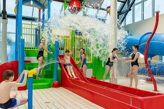 Kinder spielen auf großem Wasserspielplatz mit roten und blauen Rutschen.