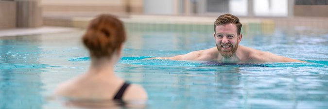 Ein Mann schwimmt lächelnd auf eine Frau im Schwimmbecken zu. 