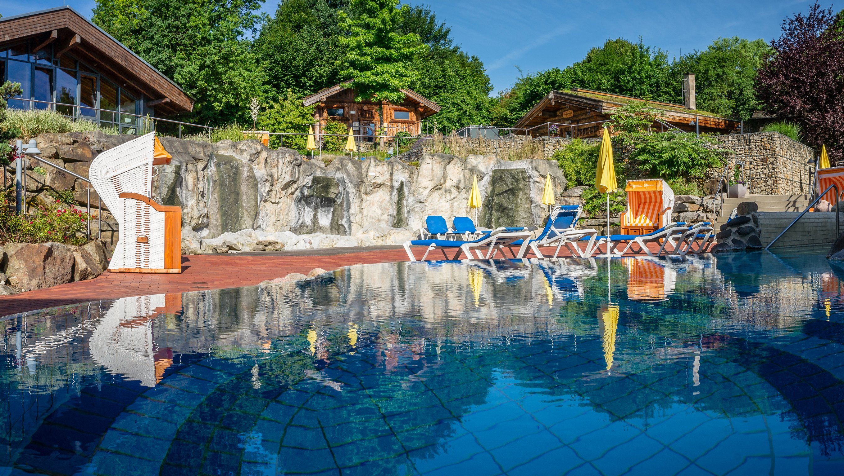 Viele Saunahäuser, davor ein blaues Entspannungsbecken im Saunagarten