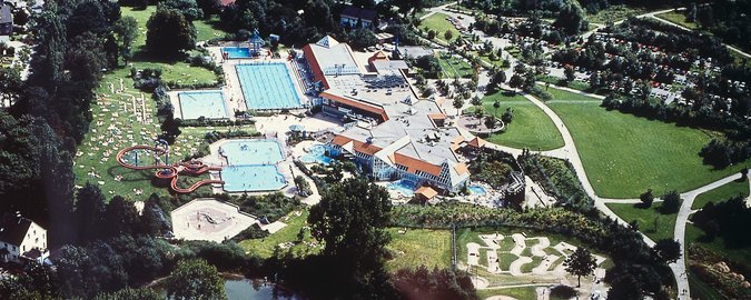 Badeanstalt von oben mit Gebäude und Außenpool neben Grünflächen und Zufahrtsweg