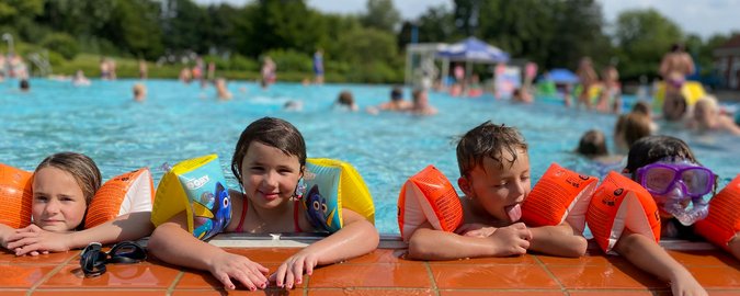 Vier Kinder lehnen in Schwimmflügeln am Beckenrand des Aussenschwimmbeckens.