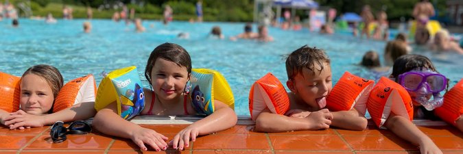 Vier Kinder lehnen in Schwimmflügeln am Beckenrand des Aussenschwimmbeckens.