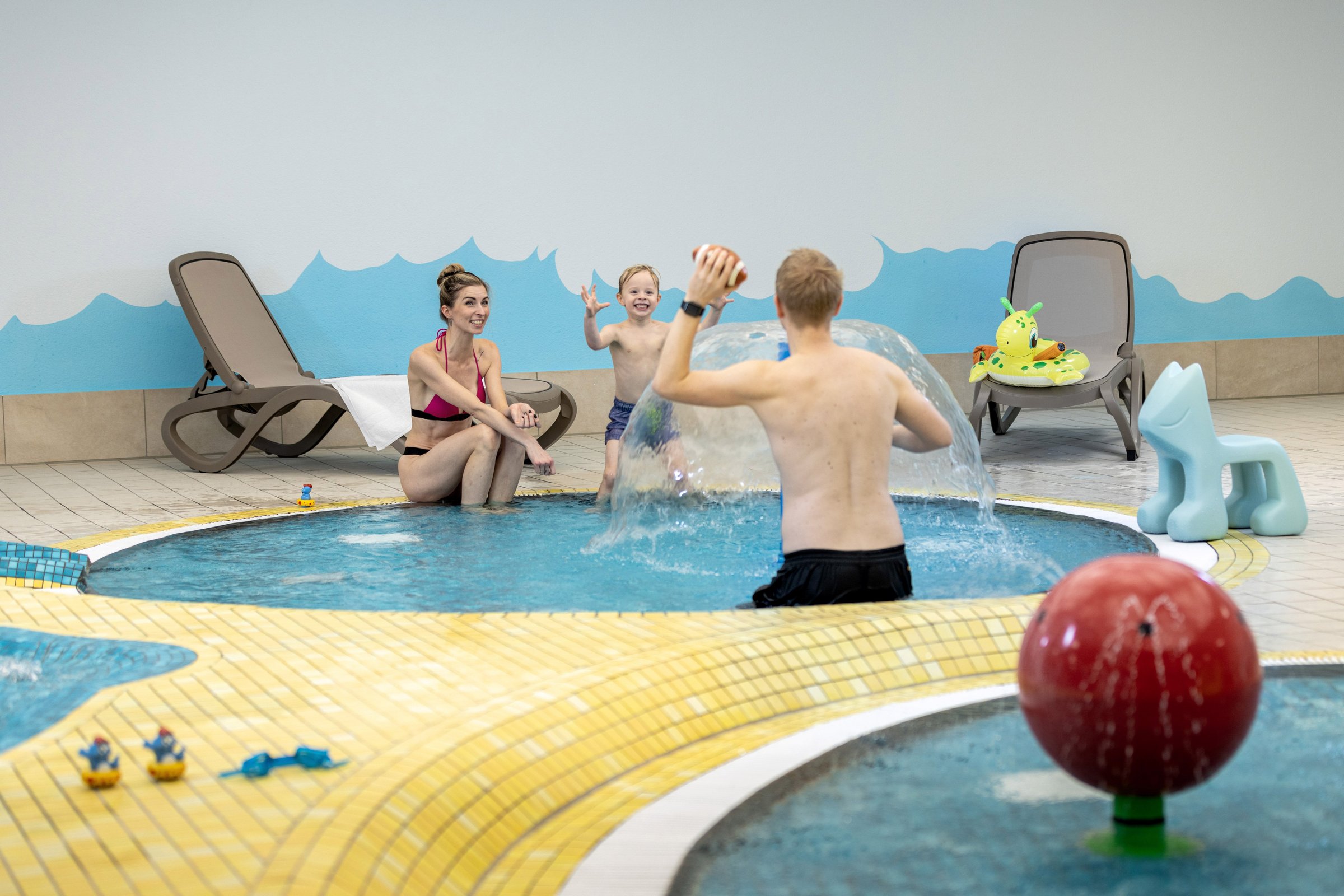 Familie spielt mit einem Football im gelb-blauen Babybereich