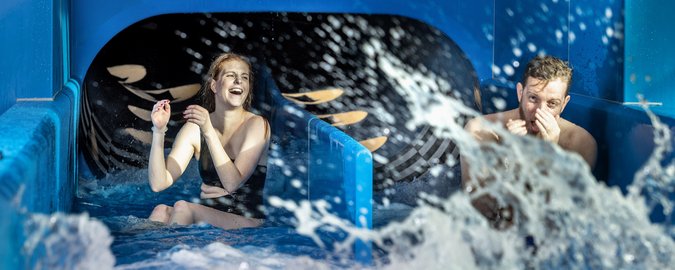 Mann und Frau kommen aus einer Wasserrutsche mit zwei unterschiedlichen Bahnen.