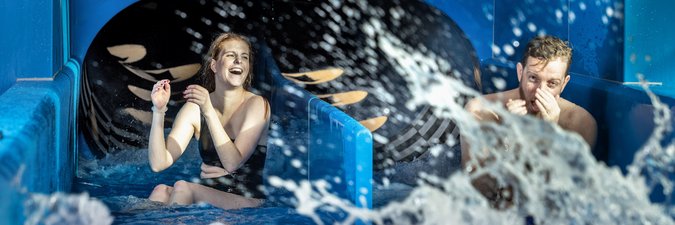 Mann und Frau kommen aus einer Wasserrutsche mit zwei unterschiedlichen Bahnen.