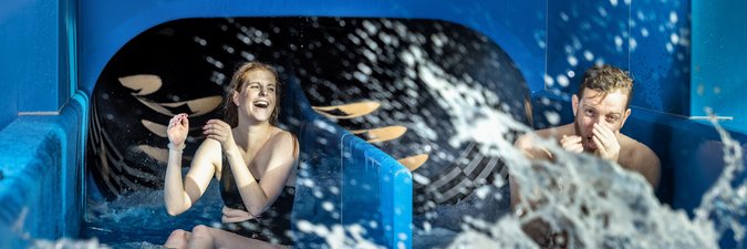 Wasserrutschen-Erlebnis für Erwachsene Mann und Frau kommen aus einer Wasserrutsche mit zwei unterschiedlichen Bahnen.