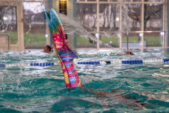 Mermaiding im Copa Ca Backum - Schwimmen wie eine Meerjungfrau Aus dem Wasser ragt eine Meerjungfrau-Schwimmflosse und Wasser spritzt umher