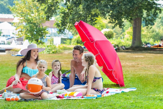 Eine Familie picknickt auf der Liegewiese des Freibad Backums bei strahlendem Sonnenschein.