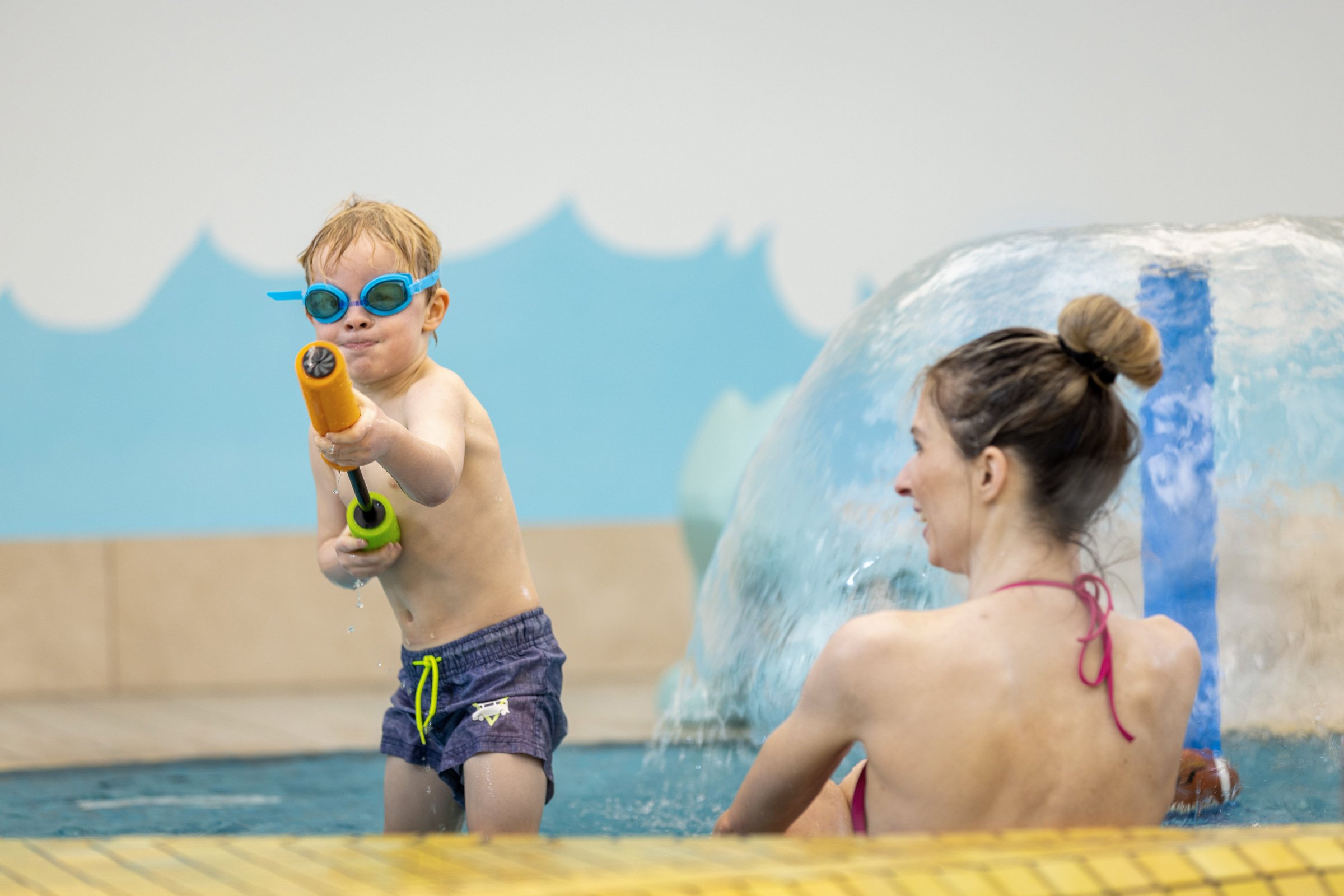 Ein kleiner Junge hält eine Wasserpistole auf die Kamera gerichtet. 