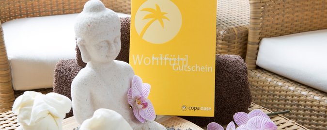 Weiße, kleine Buddhafigur sitzt auf Rattan-Tisch vor einem gelben Infoprospekt.