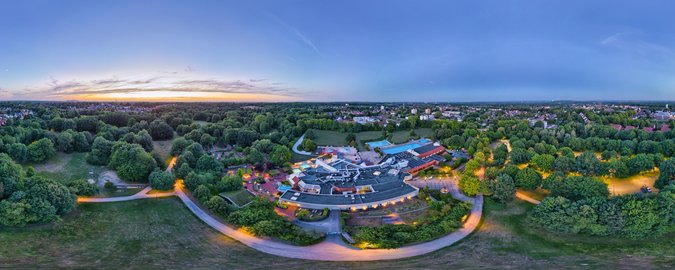 Panorama-Blick des copa ca backum Schwimmbads aus der Vogelperspektive. Panorama-Blick auf ein Schwimmbad, ansässig mitten zwischen Wäldern und Wiesen, im Hintergund erkennt man eine Stadt.