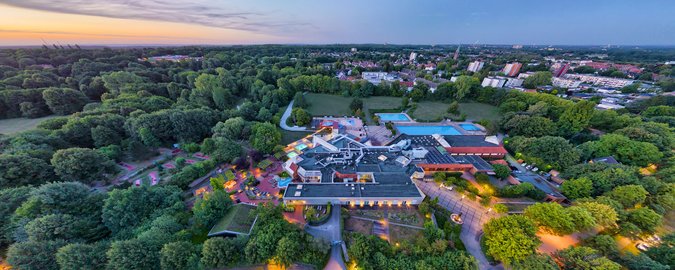 Weitwinkel-Blick auf ein Schwimmbad, ansässig mitten zwischen Wäldern und Wiesen, im Hintergund erkennt man eine Stadt zur Abenddämmerung.